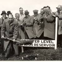 Start of work on Avon Dam, showing officials standing near top water level marker and the first clod