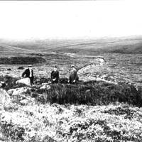 Three men sitting in hut circle on Erme Plains
